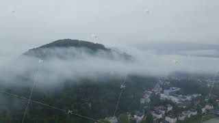 Aerial view of low hanging clouds moving over Kapuzinerberg mountain with the Salzach River and city [upl. by Sivrahc]